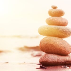 Stones Pyramid on Sand Symbolizing Zen, Harmony, Balance. Ocean at Sunset in the Background