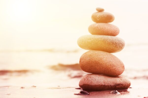 Stones Pyramid on Sand Symbolizing Zen, Harmony, Balance. Ocean at Sunset in the Background